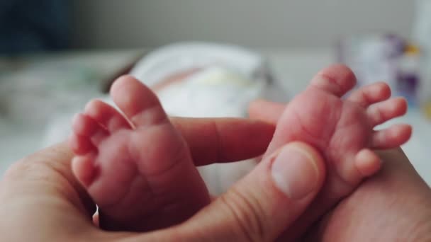 Pequeños pies de un bebé recién nacido en manos de su padre. Un recién nacido yace en un cambiador junto a la ventana. Padre e hijo. Cuidar a un niño . — Vídeo de stock