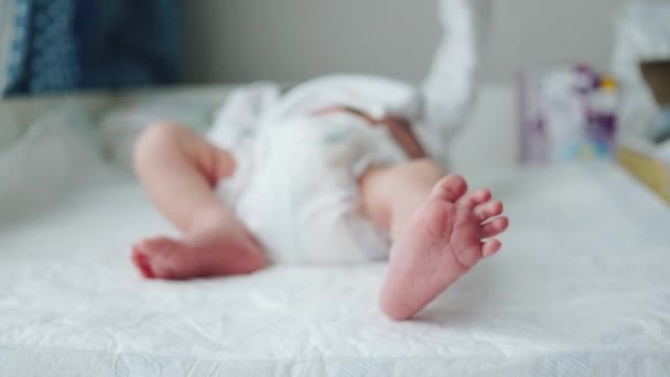 Gambe piccole di un neonato. Il bambino muove una gamba. Sfocati. Una nuova vita. Bambino nel pannolino sul tavolo fasciante in casa — Video Stock