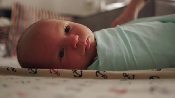 Anne yeni doğmuş bebeğini kundaklıyor. Bebeği bebek bezine sarar. Yeni doğmuş bebek yatakta yatıyor. — Stok video