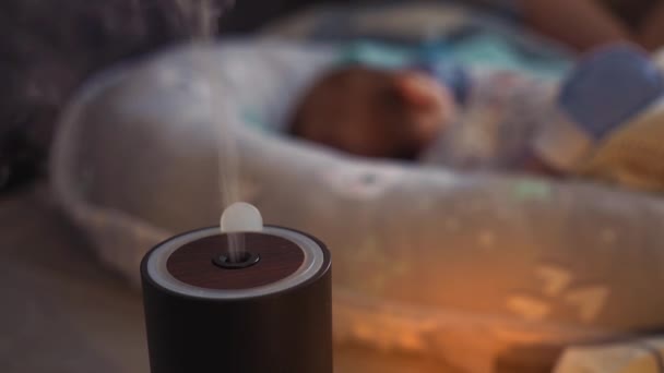 眠っている赤ん坊の前で働く加湿器から蒸気。黒い加湿器は乾燥空気を湿らせる。人々の快適さと幸福を向上させます.気候変動装置。呼吸器疾患予防. — ストック動画