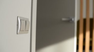 Dişi el ışık şalterine dönüyor. Yakın çekim. Arka planda kapı