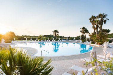 Güneş yataklı, şemsiyeli ve palmiyeli su havuzu. Lüks Panoramik Manzara. Sardunya 'da. İtalya. Gün doğumu.