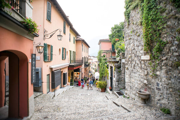 Bellagio. Lake Como. Italy - July 20, 2019: Amazing Old Narrow Street in Bellagio. Lake Como, Italy, Europe. Famous Picturesque Cobblestone Street with Souvenir Shops, Restaurants and Cafes.