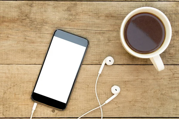 Kulaklıklar ve ahşap masa kahve ile Smartphone. Beyaz ekran.