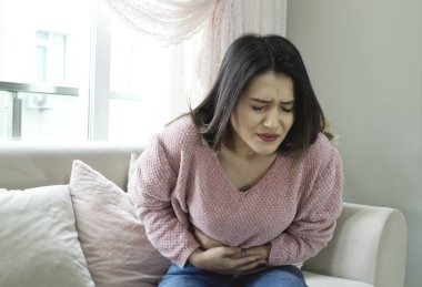 Mide ağrısı evde acı kanepede oturan genç kadın.