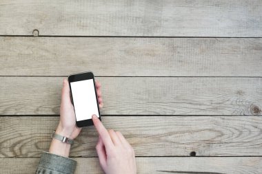 Boş ekran ile akıllı telefon üzerinde ahşap masa holding kadın eller.