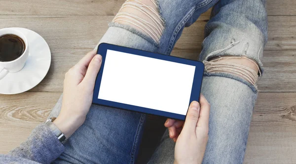 Digital tablet in woman hands sitting on a wooden floor.