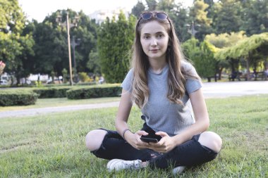 Parkta akıllı telefon kullanan genç bir kadın..