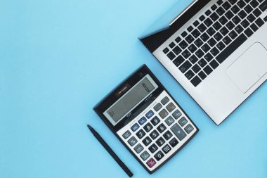 Dizüstü bilgisayar, hesap makinesi ve kalem mavi bir arka plan üzerinde.