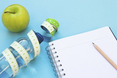 Taze elma, bant, su şişesi ve mavi arka plan üstünde defter ölçme.