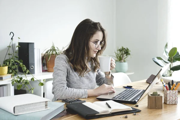 Kahve fincanı Office ile dizüstü bilgisayar üzerinde çalışan genç iş kadını.
