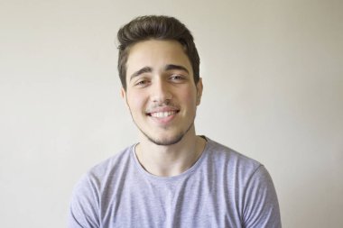 Gri arka plan üzerinde izole kamera bakarak gülümseyen yakışıklı adam portresi.