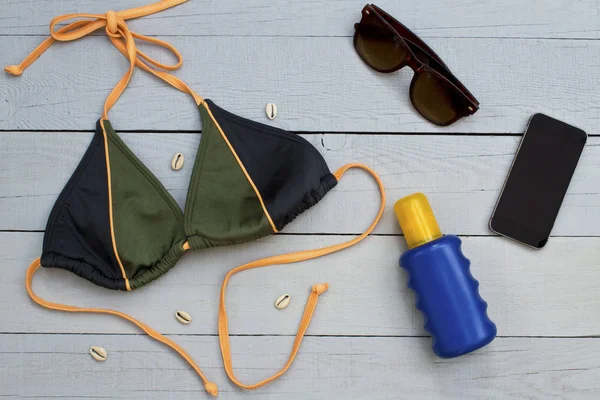 Bikini, güneş kremi, güneş gözlüğü ve ahşap arka plan üzerinde cep telefonu.