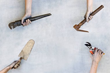 Gri arka plan üzerinde inşaat araçlarını tutan eller.