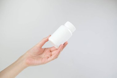 Gri arka planda beyaz plastik şişe tutan kadın..