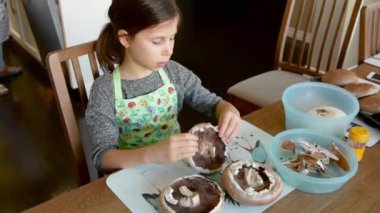 Kız mantarları kızartılması için hazırlıyor, derinin kapaklarını temizliyor ve bir kaseye koyuyor.