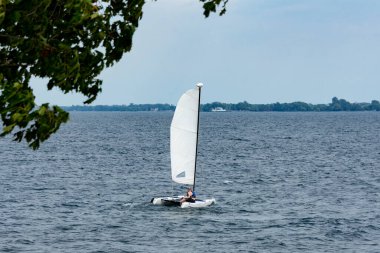 Bir adam katamaranla gölün karşı kıyısına gidiyor.