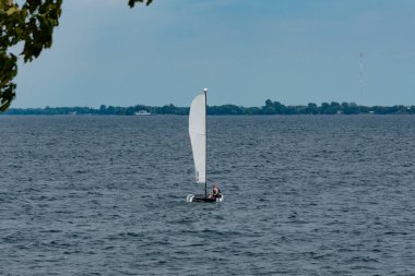 Bir adam katamaranla gölün karşı kıyısına gidiyor.