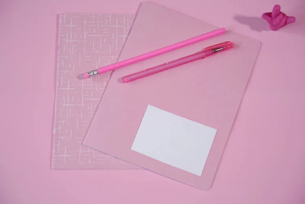 pink notebook and pink pen with a pencil, an eraser in the form of a hand showing a good luck sign on a pink background with copy space for text