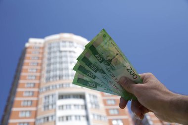 Erkek el yüksek bir binanın arka planda yeni Rus banknotları iki yüz ruble tutar ve mavi bir gökyüzü.