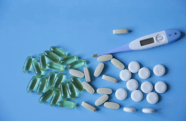 pills, capsules and a electronic thermometer for measuring body temperature on a blue background, with copy space, flat lay