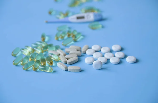 pills, capsules and a electronic thermometer for measuring body temperature in soft blur on a blue background, with copy space