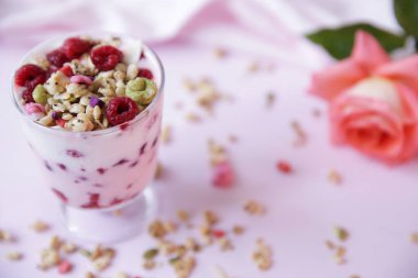 Taze ahududulu yoğurt ve açık pembe arka planda gül. Sağlıklı yiyecekler. Metin için kopyalama alanı ile.