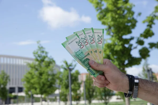 Hand holding a new Russian banknote two hundred rubles on the background of a blue sky and green foliage. Cash paper money