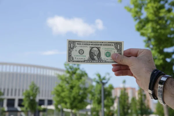 Dollar in hand against the background of the building of blue sky and green foliage. Paper Cash. With copy space.