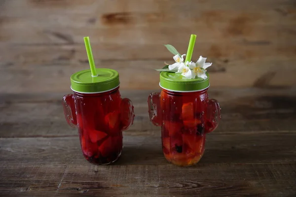 Red sangria of fresh berries and citrus fruits in a glass with a drinking straw and a flower on a table made of natural wood. Fresh summer drink. With copy space.