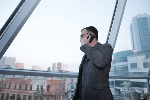 Young Businessman Glasses Jacket Talking Mobile Phone Office Panoramic Window — Stock Photo, Image