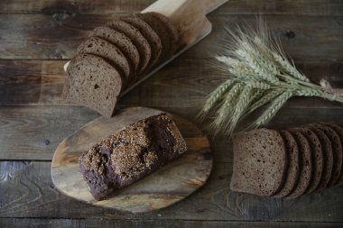 Bütün ve dilimlenmiş çavdar ekmeği susam tohumu ve çavdar ekmeği ile ahşap bir arka planda. Düz yatıyordu.