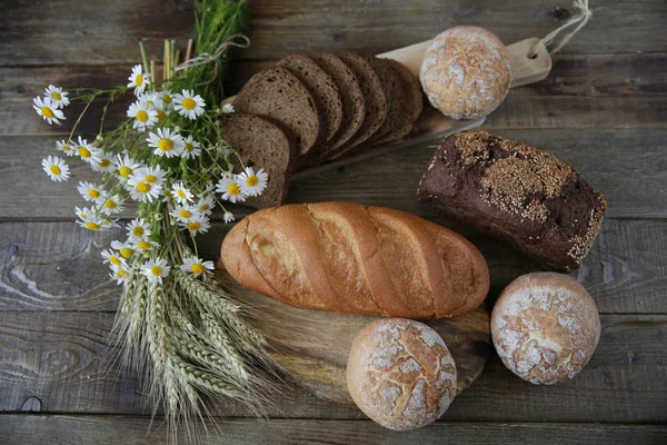 susam ve çörekler ve rustik ahşap arka plan üzerinde kulakları ve çiçekleri ile beyaz ekmek bir somun ile çavdar ekmeği natürmort, üst görünüm, düz yatıyordu