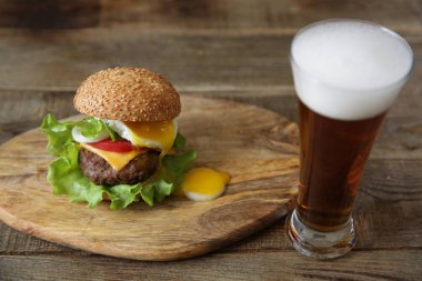 Sebze, domates sosu ve kızarmış yumurta ile sığır cutlet ile hamburger güzel akan sarısı ve metin için kopya alanı ile ahşap rustik arka planda bir bardak bira.