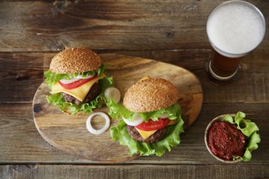 Peynir, turşu, domates, soğan, marul ve domates sosu ile iki Burger metin için kopya alanı ile ahşap rustik arka planda bir bardak bira ile bir fincan. Üst görünüm. Düz yatma.