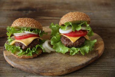  Peynir, Pickles, domates, soğan, marul ve domates sos ile sığır cutlet ile iki hamburger metin için kopya alanı ile ahşap rustik arka planda bir daire içinde.