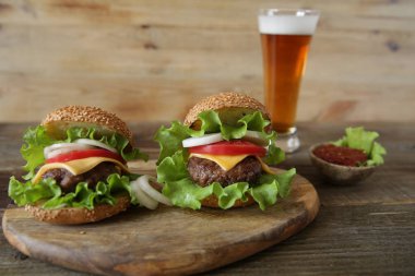  Peynir, turşu, domates, soğan, marul ve domates sosu ile sığır köftesi ile iki hamburger metin için kopya alanı ile ahşap rustik arka planda bir bardak bira ile bir fincan.