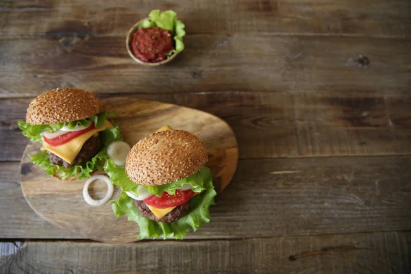 Two hamburger with beef patty, with cheese, tomatoes, onions, lettuce and tomato sauce in a saucer on a wooden rustic background with copy space for text. Top view. Flat lay.