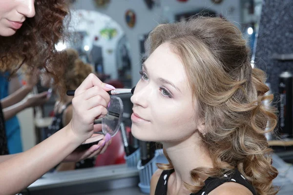 Professional makeup artist applying makeup brush on the face of a young blonde woman in a Beauty Salon. Makeup for the bride and lady. Wedding makeup artist.