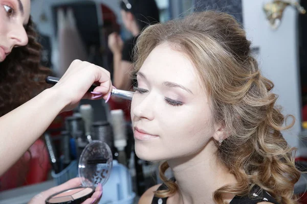 Professional makeup artist applying makeup brush on the face of a young blonde woman in a Beauty Salon. Makeup for the bride and lady. Wedding makeup artist.