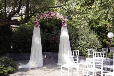 Gelin ve damat için havadan ipek kumaşla çok renkli çiçekler ve güller bir düğün kemer yeşil bir ağaç altında duruyor. Açık havada düğün töreni. Düğün konsepti. Botanik tarzı. Uyum konseptinde istirahat.