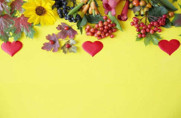 Autumn composition with red heart. Maple leaves, flowers and rowan berries on yellow background. Autumn, fall, Valentine, halloween, thanksgiving day concept. Flat lay, top view, copy space.