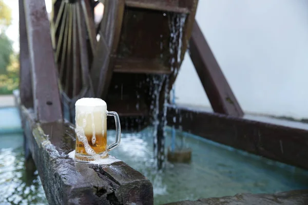落ちる水と木製のミルホイールの背景に天然の木製のボード上の泡とビールのガラス パターン バナー — ストック写真