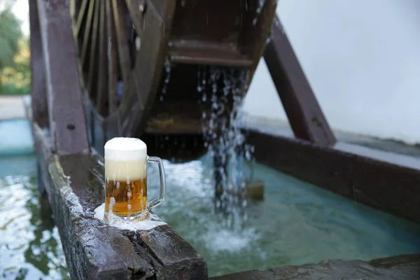落ちる水と木製のミルホイールの背景に天然の木製のボード上の泡とビールのガラス パターン バナー — ストック写真