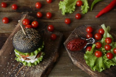 Siyah sandviç, hamburger ya da hamburger sığır eti ya da tavuk, domates, soğan, peynir, marul ve tahta tahta üzerinde susamlı çörek. Fast food konsepti. Üst görünüm