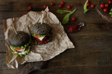 İki büyük siyah sandviç, hamburger ya da hamburger sığır eti ya da tavuk, domates, peynir, marul ve tahtadan bir masada susamlı çörek. Fast food konsepti. Üst görünüm.