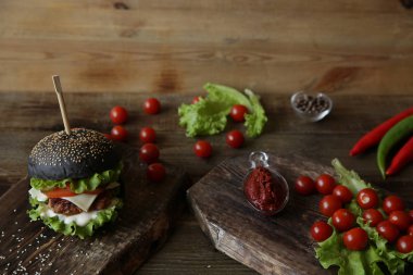 Siyah sandviç, hamburger, hamburger veya tavuk, domates, soğan, biber, peynir, marul ve tahtadan yapılmış susamlı ekmek. Fast food konsepti. Metin için kopyalama alanı ile