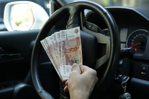 Hand with money. Banknotes five thousand Russian rubles in the hand on the steering wheel of a car. Cash paper money. Five thousandth bill. Auto industry