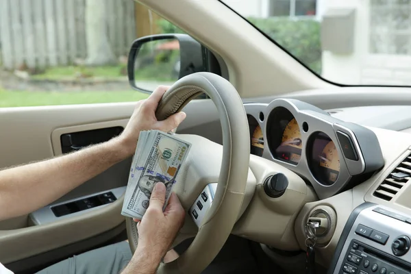 hand holds one hundred dollar bills in cash against the background of a steering wheel of a car. Concept of sale, purchase and leasing of cars.