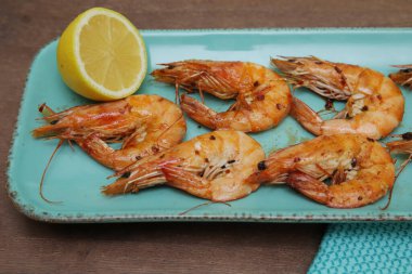 Ahşap arka planda mavi tabakta limonlu kızarmış karides ve kumaş peçete. Pankart, menü, poster. Boşluğu kopyala.